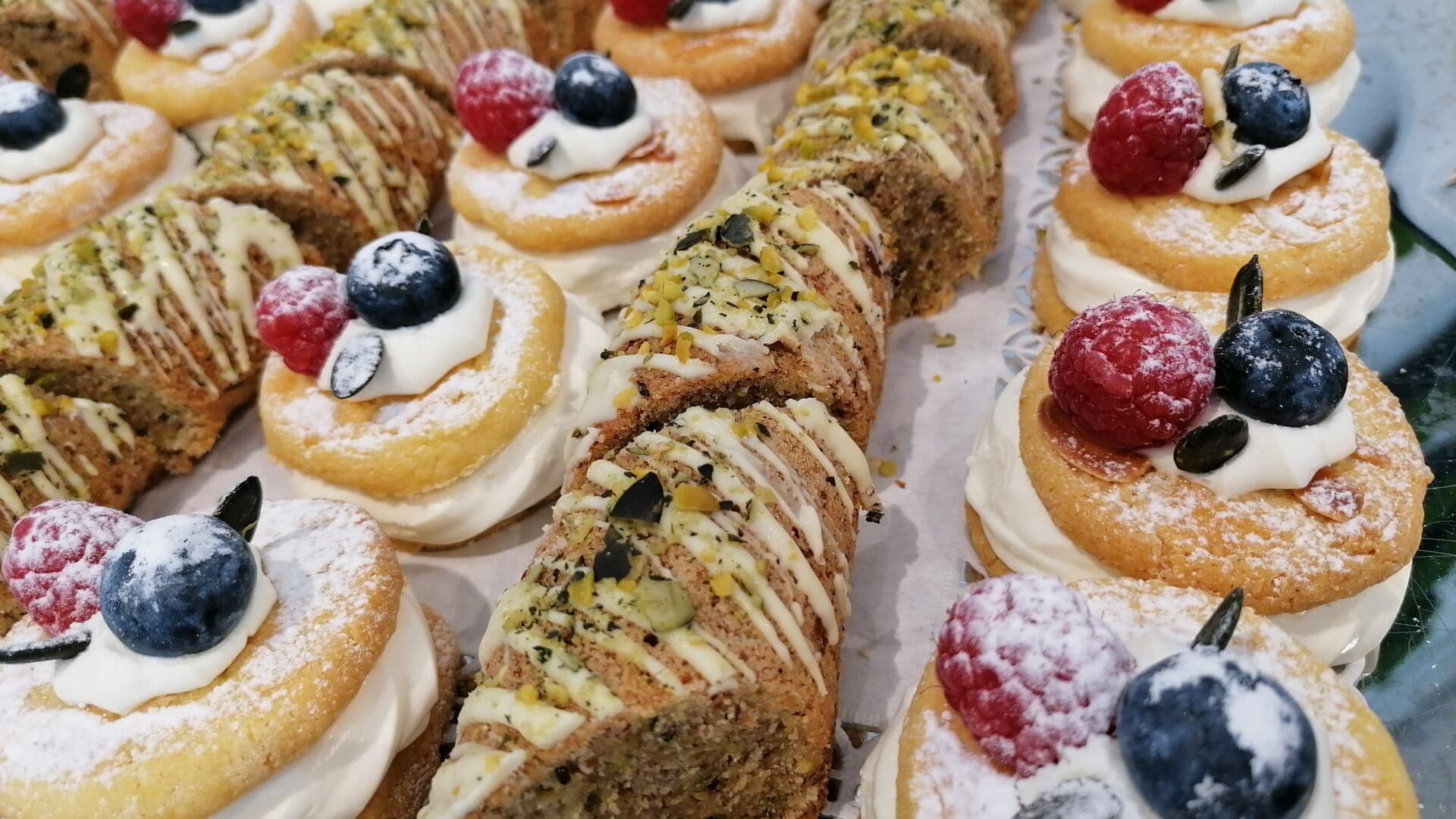Zitronencreme-Kekse 1 Ein Tablett mit verschiedenen Mehlspeisen im Das Gxund in Bad Hofgastein: runde, mit Sahne gefüllte Biskuitböden mit Blaubeeren und Himbeeren sowie dreieckige, mit Zuckerguss und gehackten Pistazien bestrichene Scheiben.
